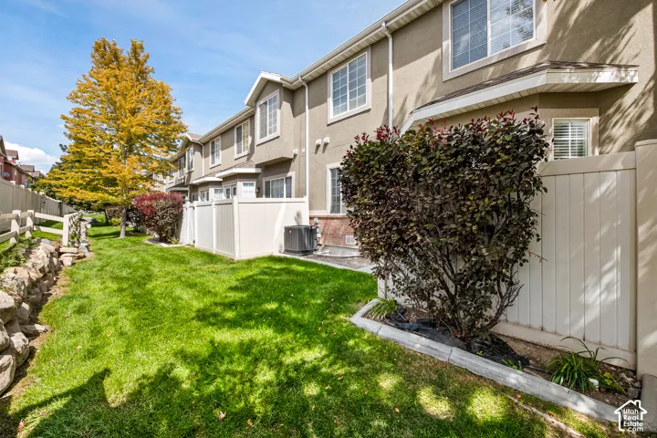 Rear exterior featuring a green lawn, established landscaping, and privacy fencing