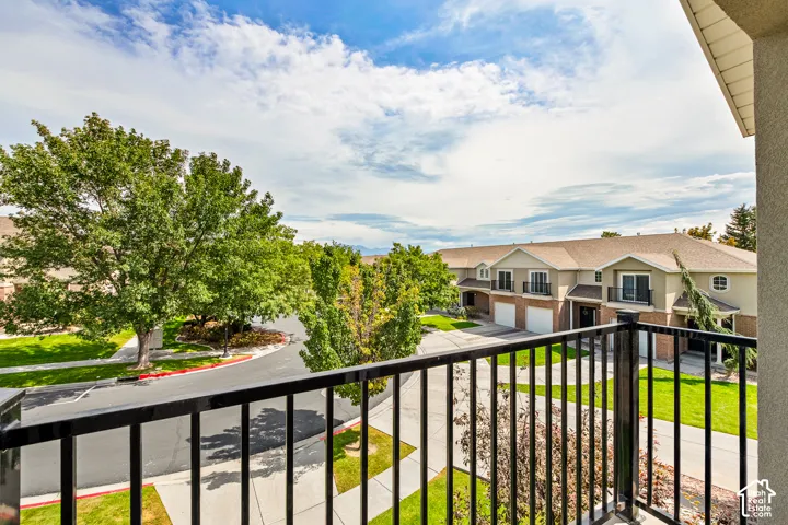Balcony with black metal railing overlooking a residential street with mature trees and manicured lawns