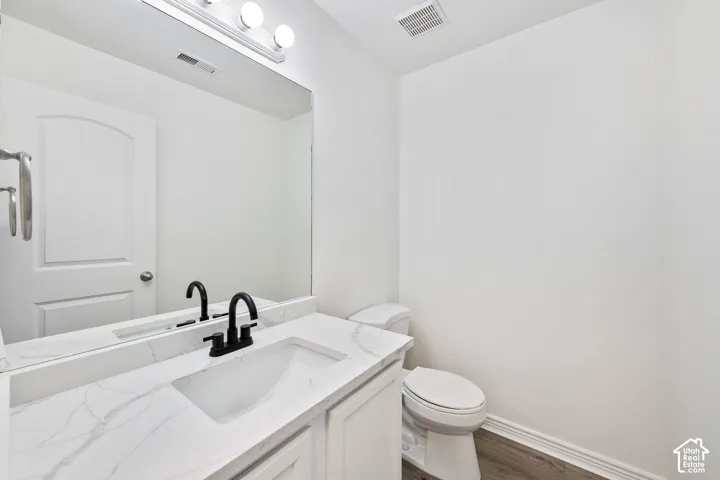 Vanity with integrated sink and matte black faucet, wall-mounted mirror, white toilet, and wood-finish flooring