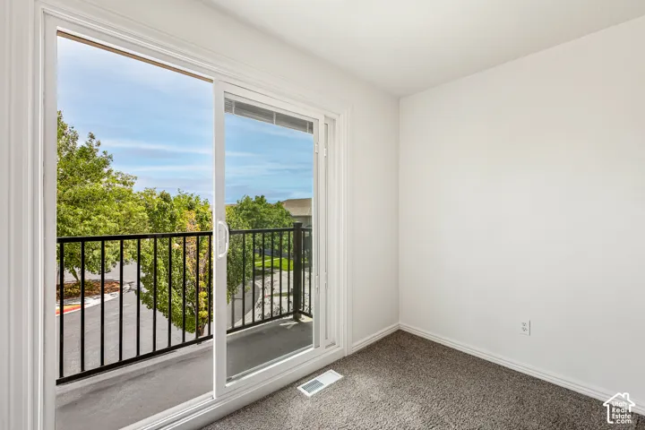 Sliding glass door leading to a balcony with black metal railings, neutral wall paint, and gray carpet flooring