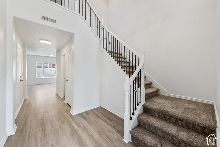 Two-story entryway with wood-finish flooring, a carpeted staircase, and decorative wrought iron balusters