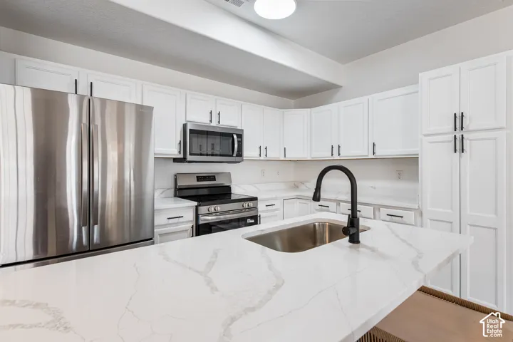 White shaker cabinetry with black hardware, stainless steel appliances, white countertops with veining, an undermount sink, and a black gooseneck faucet