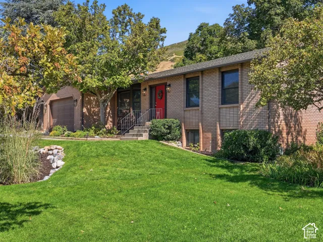 Brick exterior with a red entry door, attached garage, and mature landscaping