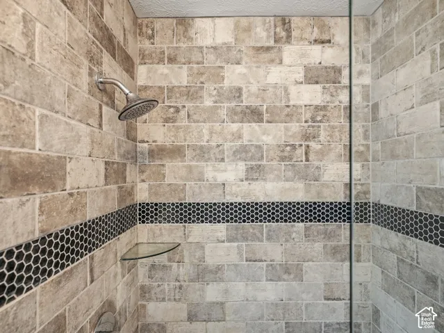 Tiled shower enclosure featuring a satin nickel showerhead, decorative mosaic tile accent band, and a clear glass corner shelf