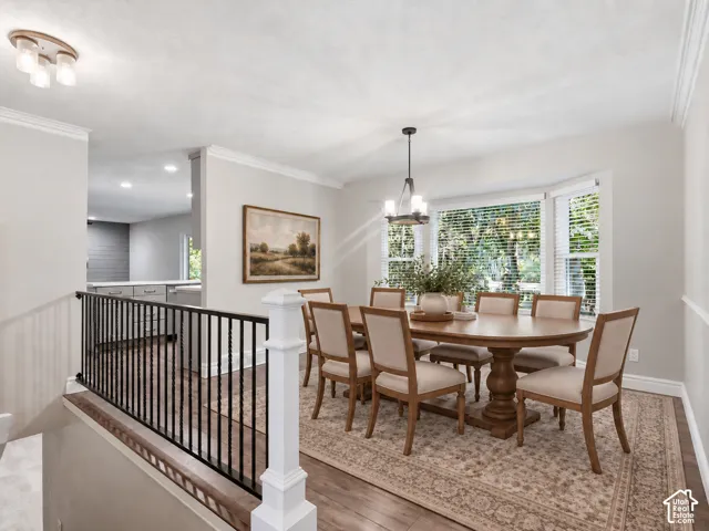 Dining area with wood-finish flooring, a bay window with blinds, and crown molding