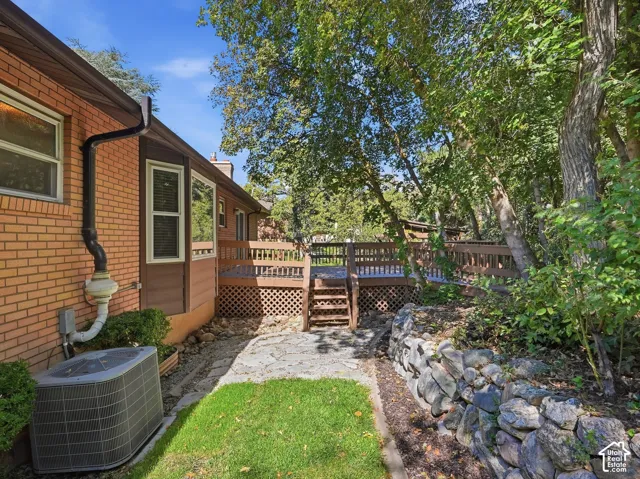 Brick exterior with a multi-level wood deck, stone retaining wall, and mature trees