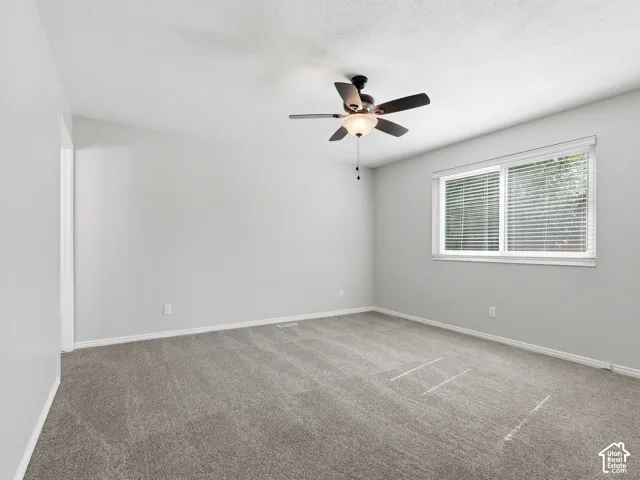 Neutral-toned wall paint, textured ceiling, gray carpeting, dual-pane window with blinds, ceiling fan with integrated lighting
