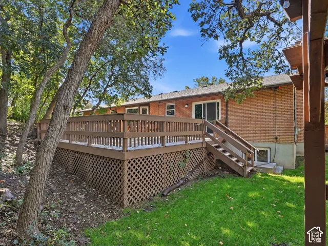 Expansive wood deck with lattice skirting, direct access to the interior via sliding glass doors, and a separate staircase leading to a grass lawn