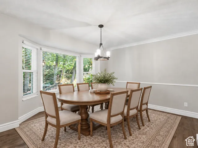 Bay window with natural light, wood-finish flooring, crown molding, and a contemporary chandelier