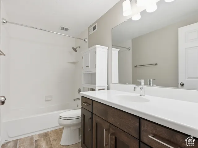 White bathtub with shower, dark wood-finish vanity with white countertop, chrome faucet, white built-in storage cabinet, and wood-finish flooring