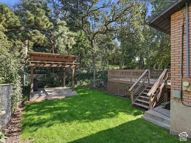 Expansive green lawn with a wooden pergola, concrete pad, and multi-level wood deck