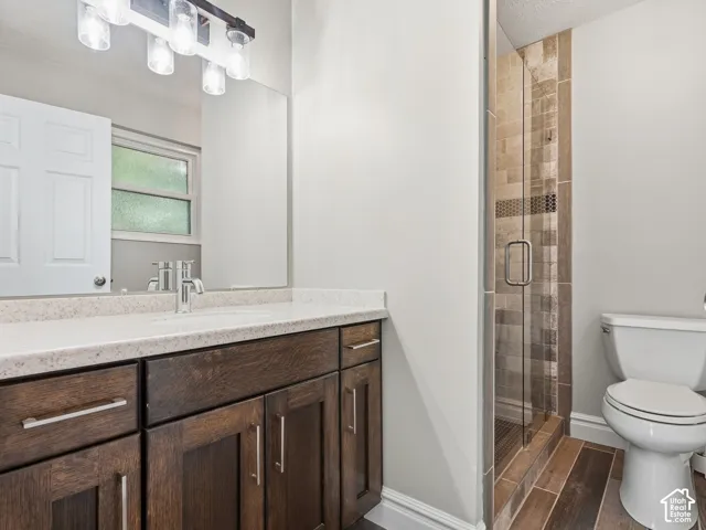 Wood-finish flooring, glass-enclosed shower with tiled surround, single vanity with light-colored countertop, and dark wood cabinetry