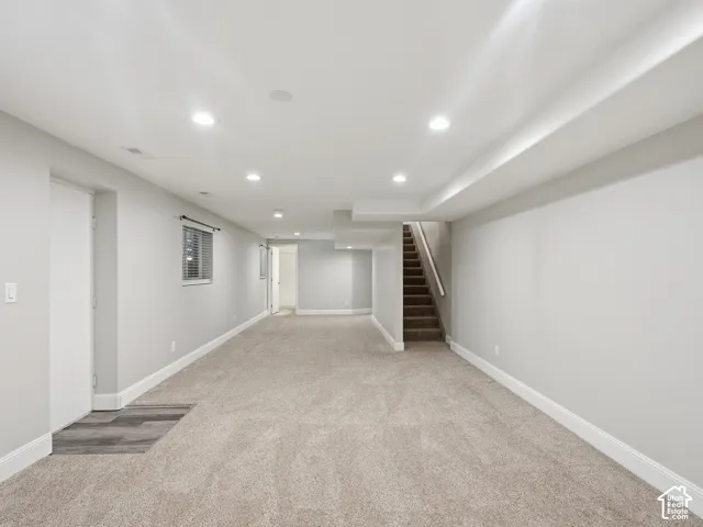 Expansive carpeted area with recessed lighting, a window with blinds, and wood-finish flooring at the entrance