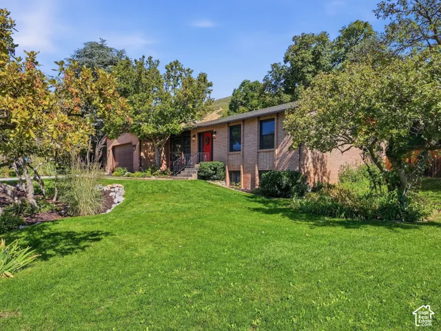 Brick exterior with a red entry door, attached garage, stone retaining wall, and mature landscaping