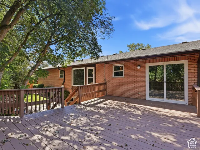 Expansive outdoor deck with wood-finish planks, integrating with brick exterior and mature trees