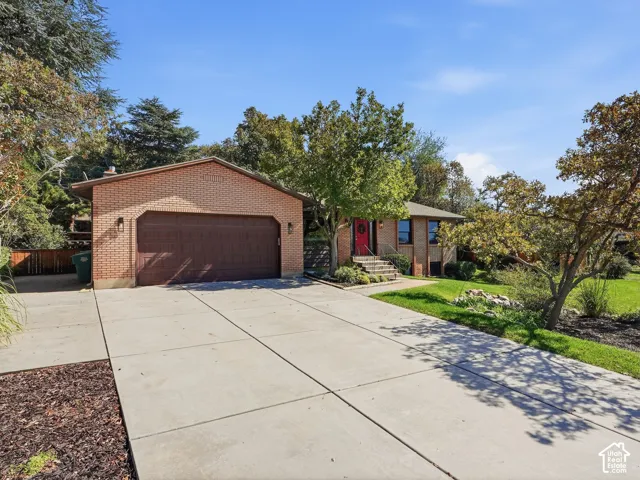 Brick facade residence with an attached garage, concrete driveway, and front landscaping