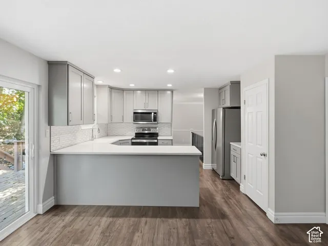 Modern kitchen featuring gray cabinetry, stainless steel appliances, white subway tile backsplash, light-toned countertops, and wood-finish flooring