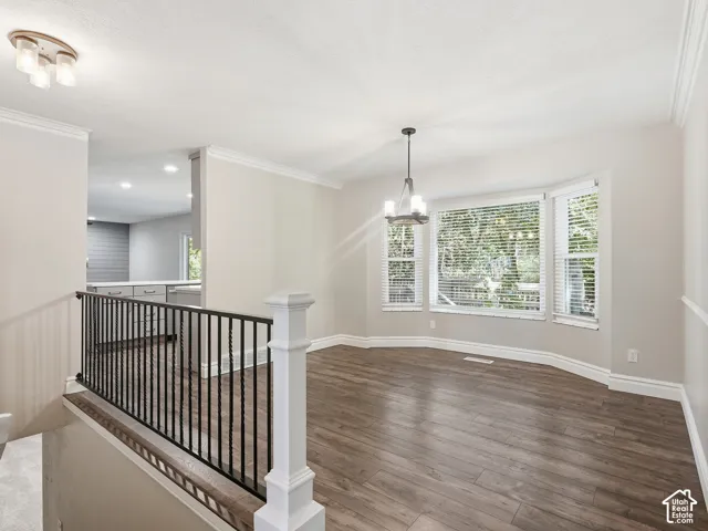 Wood-finish flooring, bay window with blinds, crown molding, and a black wrought iron railing