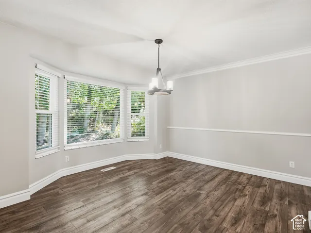 Bay window offering ample natural light, wood-finish flooring, contemporary chandelier, crown molding, and wainscoting detail