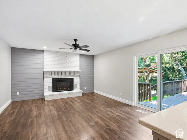 Living space featuring a white brick fireplace with a black insert, wood-finish flooring, a ceiling fan, and sliding glass doors leading to a wooden deck
