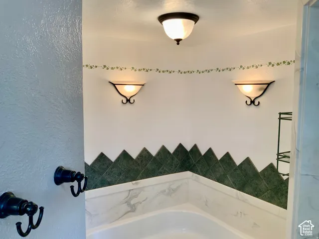 Built-in corner tub with a tile surround, wall-mounted sconce lighting, and a coordinating ceiling light fixture