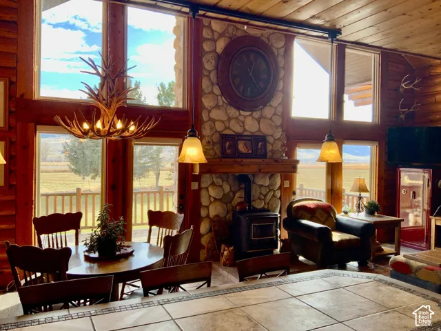 Vaulted wood-paneled ceiling, stone-clad fireplace with wood stove, antler chandelier, large picture windows, and tile flooring
