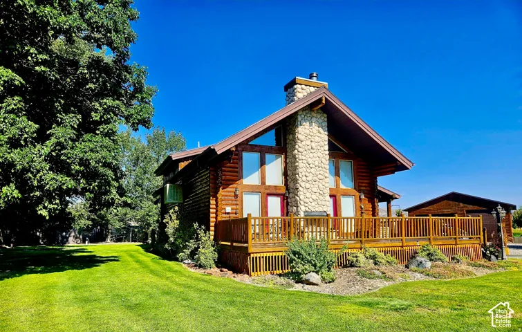 Log cabin exterior with a prominent stone chimney, a spacious wooden deck with railings, and expansive windows