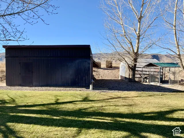 Expansive backyard featuring a manicured lawn, a dark-colored utility building with a single door, and a gravel area with additional structures
