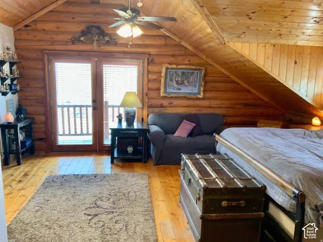 Log walls and wood-finish flooring characterize this space, featuring a vaulted wood-paneled ceiling and a ceiling fan