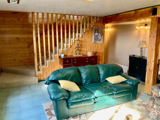 Wood-paneled wall, exposed wood beam, wood-finish staircase with carpeted treads, and tiled flooring