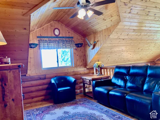 Vaulted wood-paneled ceiling, wood-plank walls, exposed log structural elements, double-pane window, and a ceiling fan with integrated lighting