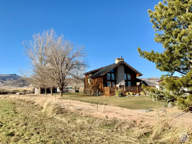 Log cabin exterior with a prominent stone chimney, A-frame roofline, expansive windows, and a raised wooden deck