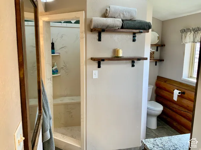 Walk-in shower with built-in bench and shelving, stone-finish flooring, wood-finish wall panels, and open shelving