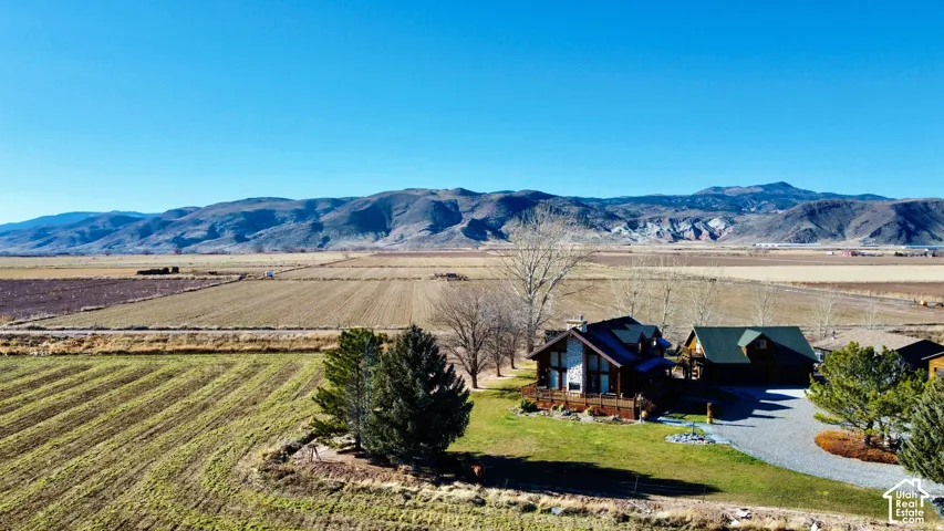 Expansive property featuring a gravel driveway, lush green lawn, mature trees, and mountain scenery
