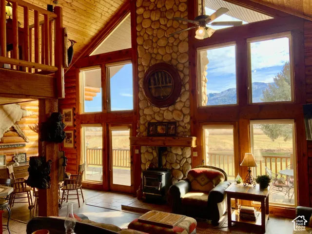Vaulted wood-paneled ceilings, a prominent river rock fireplace, expansive windows, wood-finish flooring, and a second-story open railing