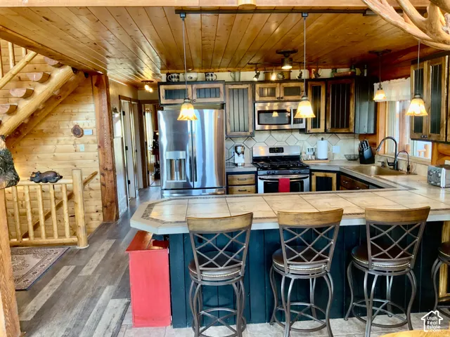 Stainless steel appliances, tile backsplash, wood-finish flooring, wood plank ceiling, and a log staircase