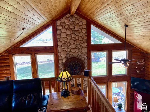 Vaulted wood-paneled ceiling, exposed wood beams, floor-to-ceiling stone-clad wall, multiple large windows, and a ceiling fan