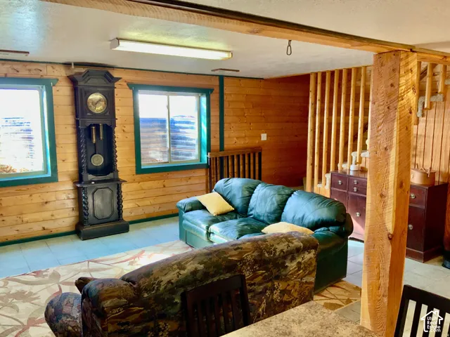 Wood-paneled walls with contrasting trim, tile flooring, exposed wood beam, and wooden staircase railing