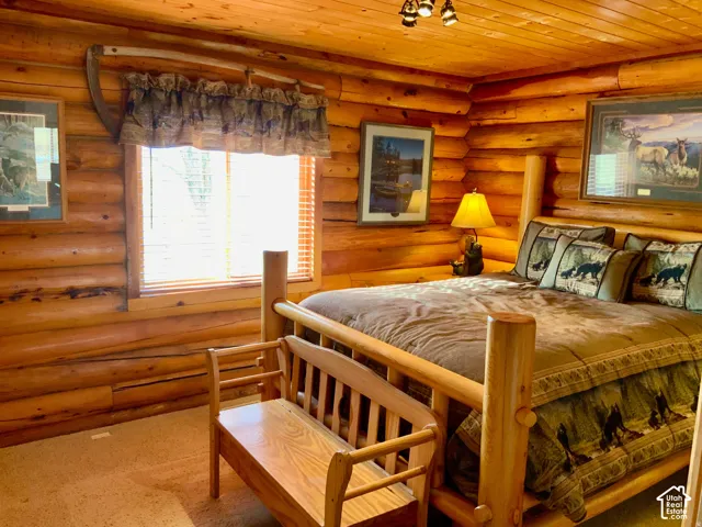 Log construction walls and ceiling, natural wood bed frame, wood bench, and recessed window with blinds