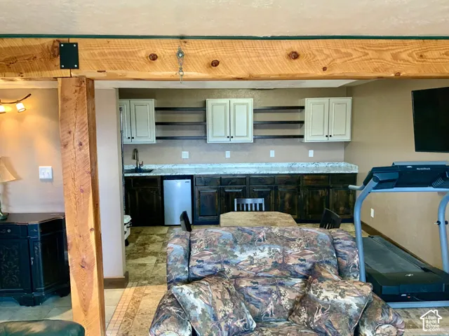 Exposed wood beam, built-in wet bar, dark wood-finish cabinetry, light-finish upper cabinets, and a tile floor
