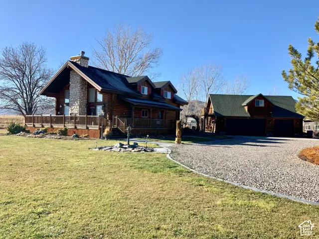 Log cabin exterior with an expansive wood deck, a prominent stone chimney, and a gravel driveway