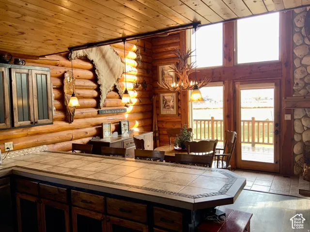 Open concept living area featuring log walls, wood-paneled ceilings, and a stone-clad fireplace
