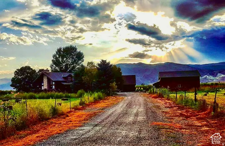 Gravel driveway leading to a residence with a stone chimney and a secondary barn structure