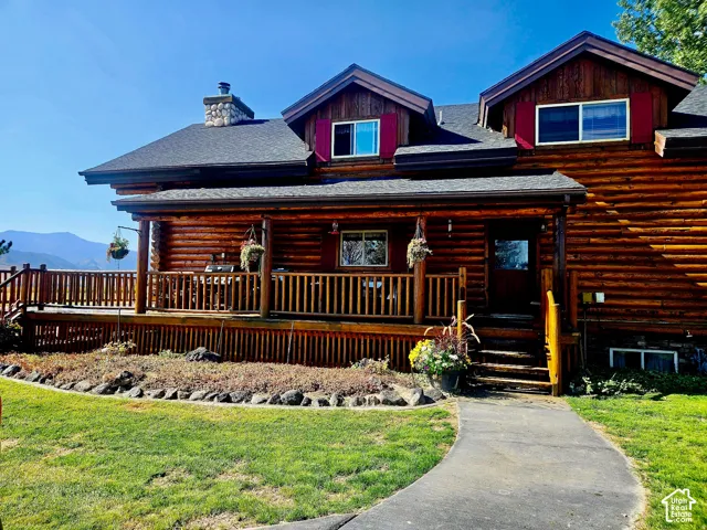 Log cabin exterior with a stone chimney, covered porch, and a multi-level wood deck