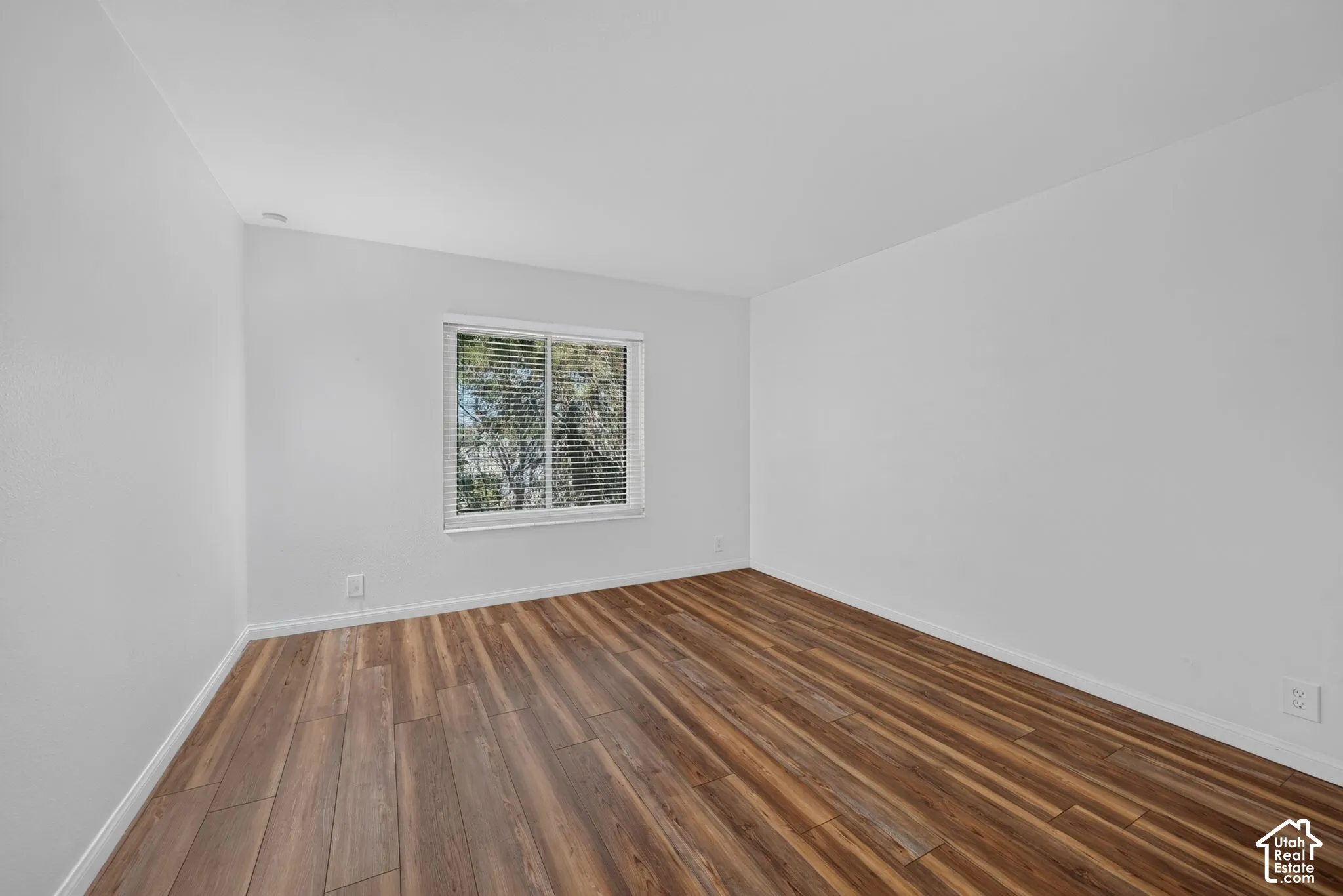 The second bedroom has laminate flooring and a window that looks out onto greenery.