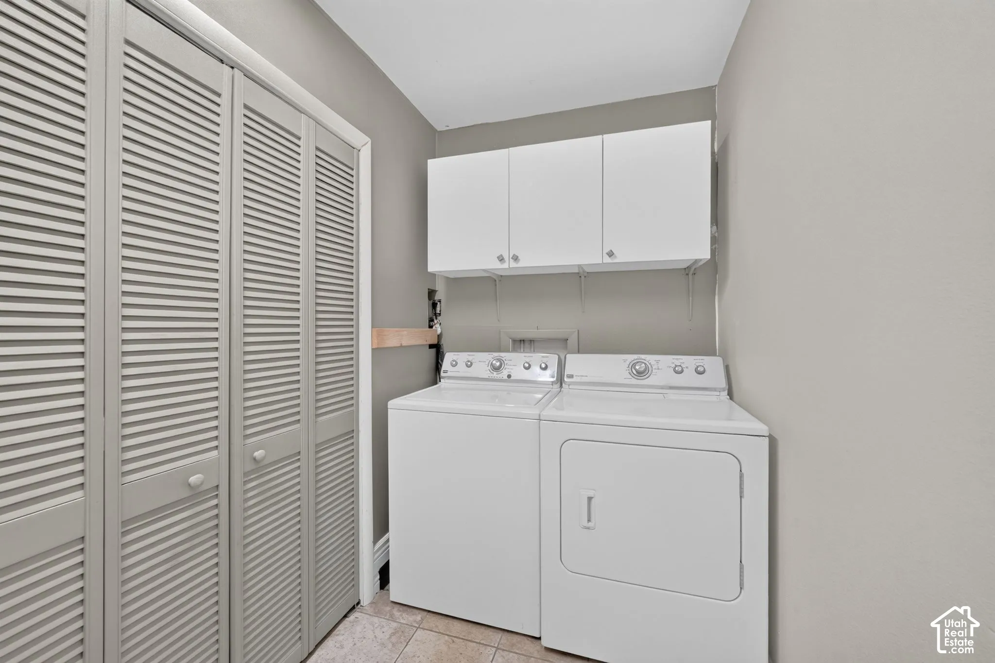 Laundry area featuring louvered bi-fold doors, upper white cabinetry, and tile flooring