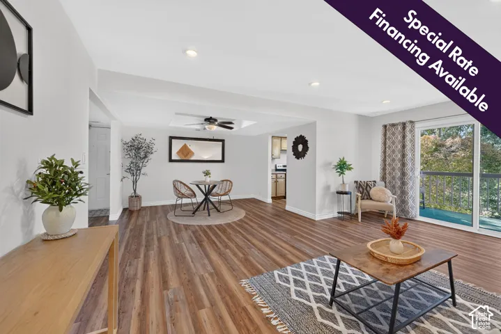 Open-concept room featuring wood-finish flooring, recessed lighting, a tray ceiling with a central ceiling fan, and sliding glass doors with access to an exterior balcony