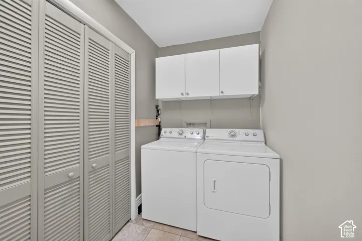 Laundry area featuring louvered bi-fold doors, upper white cabinetry, and tile flooring