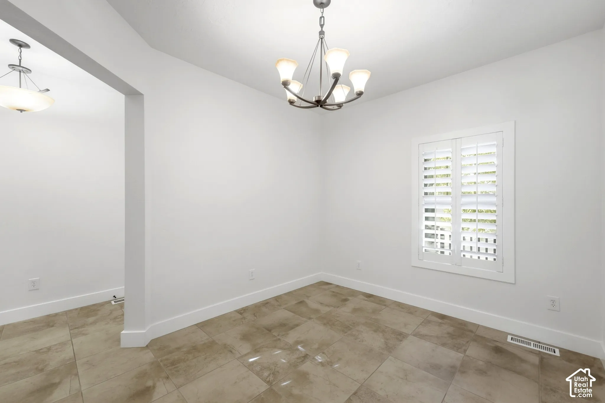 Recessed archway, ceiling-mounted light fixtures, tile flooring, window with white plantation shutters, and painted white walls