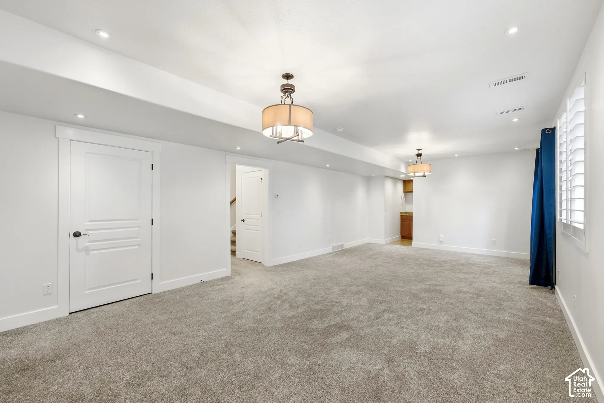 Spacious room with plush gray carpeting, recessed lighting, and two drum pendant light fixtures